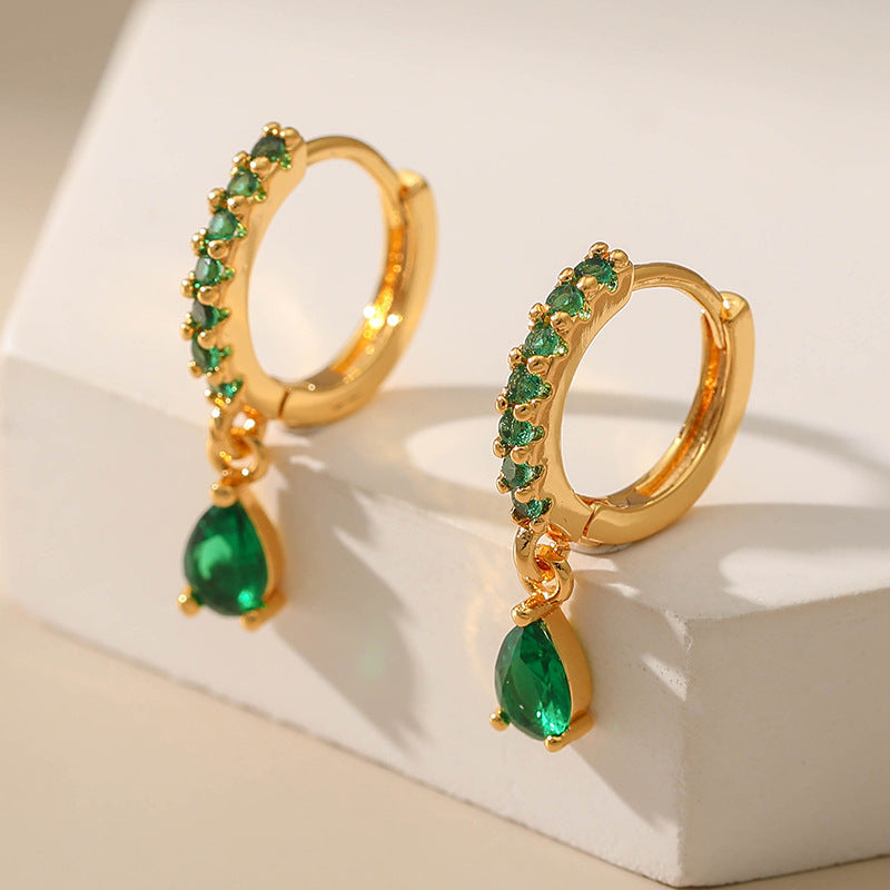Gold hoop earrings with green gemstones on a beige surface